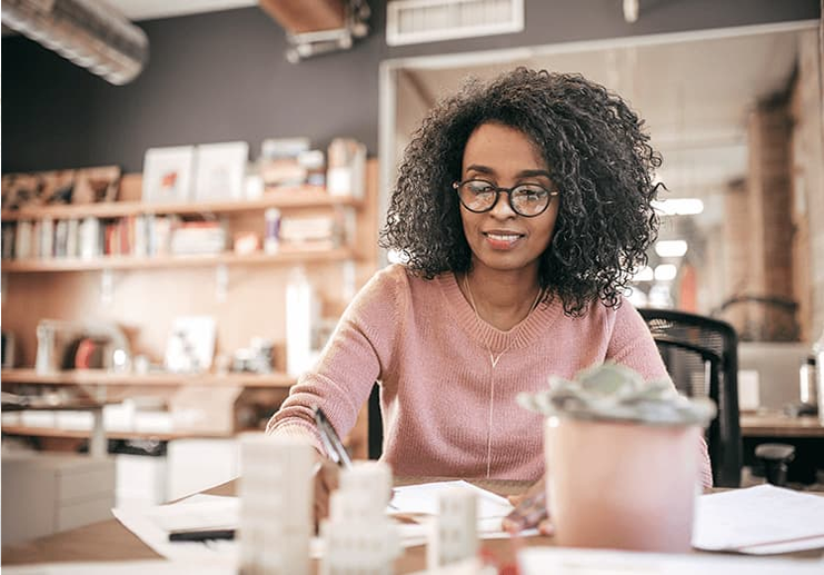 A woman with glasses works at her desk, diligently planning the growth of her pension funds in a Questrade LIRA for a secure retirement.