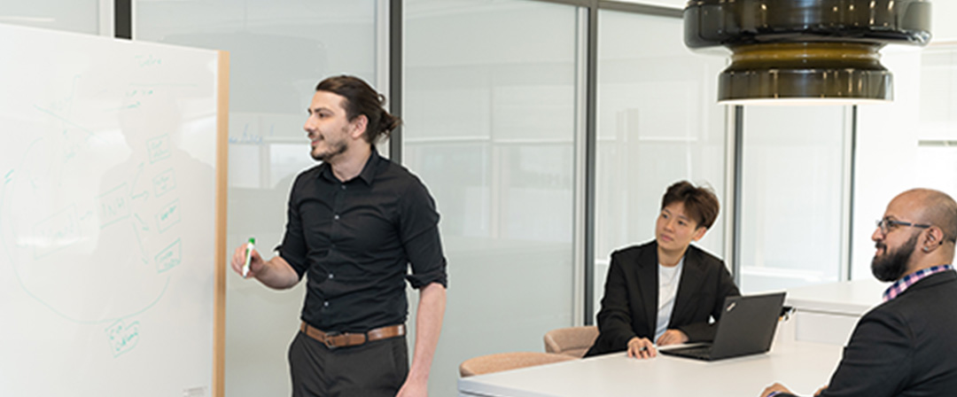 A man writing on a white board and two people paying attention